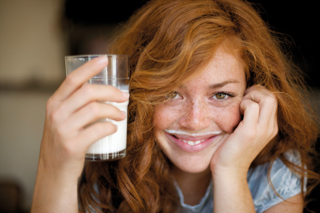 Eine Frau trinkt lächelnd ein Glas Milch, weil sie Milchprodukte wieder unbeschwert genießen kann.